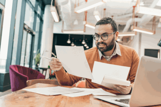 Young man in thirties reviewing documents on laptop